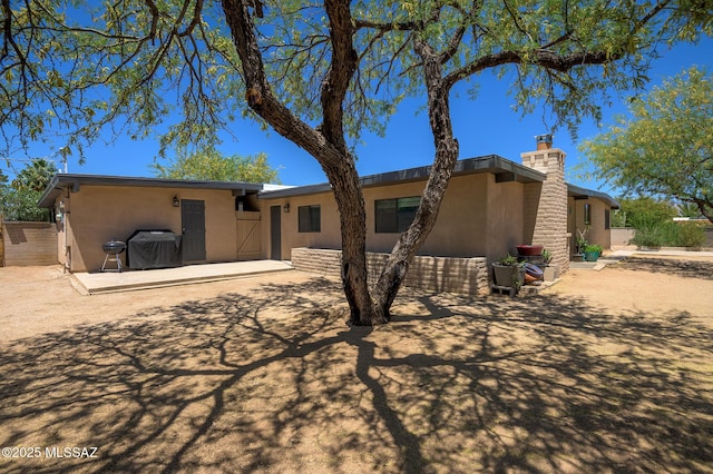 rear view of house with a patio area, stucco siding, and a chimney