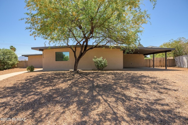 view of front of home featuring fence, stucco siding, an attached carport, and driveway