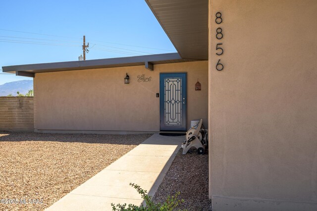 view of exterior entry with stucco siding and fence