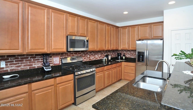 kitchen featuring a sink, dark stone counters, backsplash, and stainless steel appliances