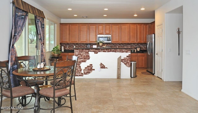 kitchen with dark countertops, brown cabinetry, stainless steel appliances, tasteful backsplash, and visible vents