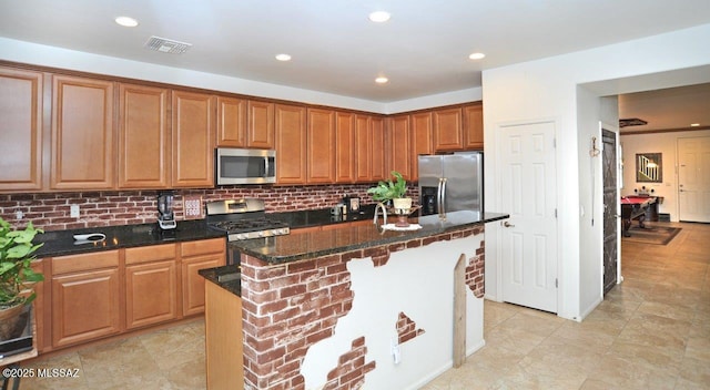 kitchen with appliances with stainless steel finishes, dark stone counters, backsplash, visible vents, and a kitchen island