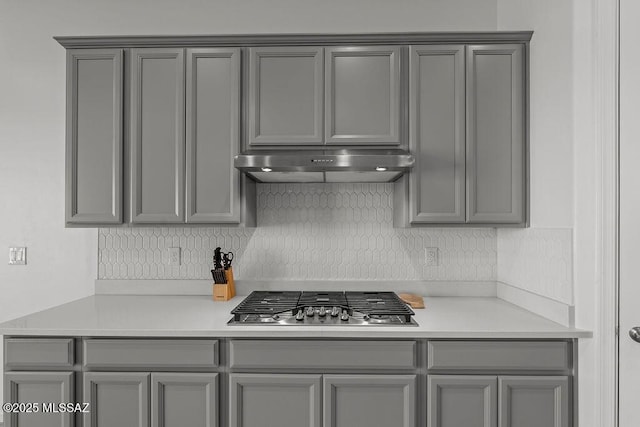 kitchen featuring stainless steel gas cooktop, light countertops, gray cabinets, decorative backsplash, and under cabinet range hood