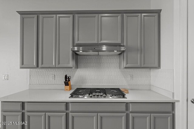 7956 S Desert Indigo Dr, Tucson, AZ 85747 - kitchen with gray cabinetry, stainless steel gas stovetop, under cabinet range hood, decorative backsplash, and light countertops