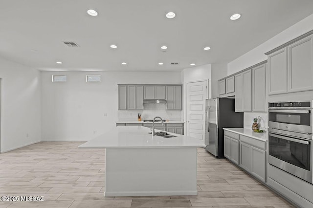 kitchen with recessed lighting, a sink, light wood finished floors, appliances with stainless steel finishes, and gray cabinetry