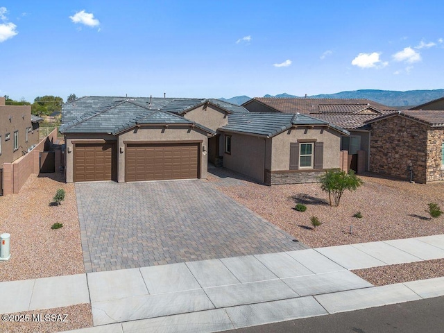 ranch-style house featuring fence, an attached garage, a tile roof, stucco siding, and decorative driveway