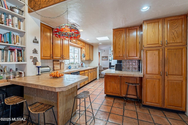 kitchen with a breakfast bar area, backsplash, a peninsula, and brown cabinetry