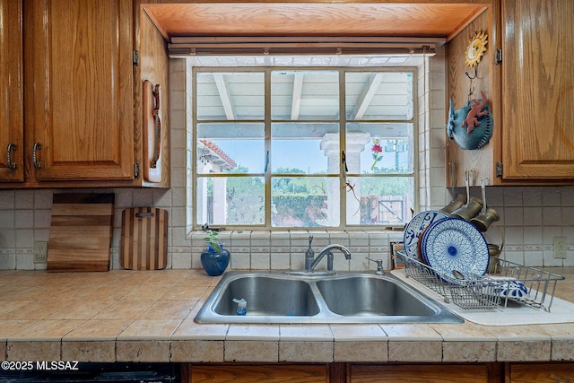 kitchen with brown cabinetry, a sink, tile countertops, and tasteful backsplash