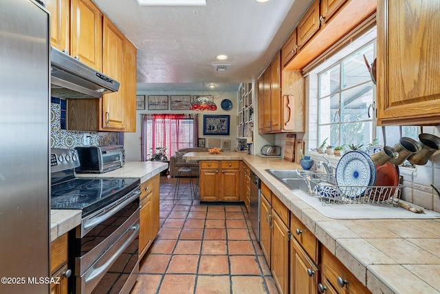 kitchen with plenty of natural light, tile countertops, tasteful backsplash, under cabinet range hood, and stainless steel appliances