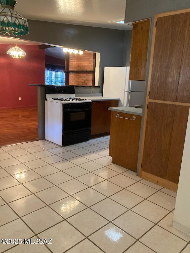 kitchen with freestanding refrigerator, light tile patterned floors, gas range, and light countertops