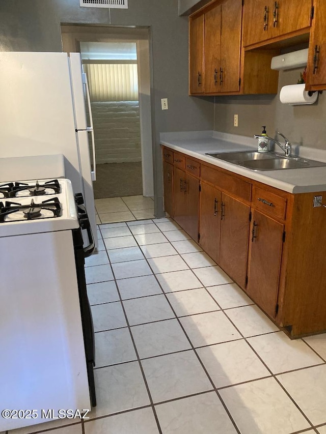 kitchen with white gas range oven, a sink, light tile patterned floors, and light countertops