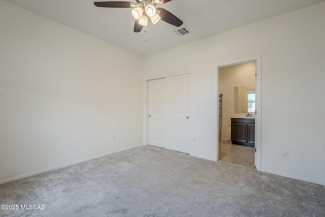 unfurnished bedroom with visible vents, a closet, baseboards, light colored carpet, and ensuite bath