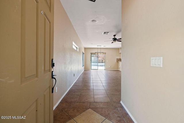 hallway with dark tile patterned floors, baseboards, and visible vents