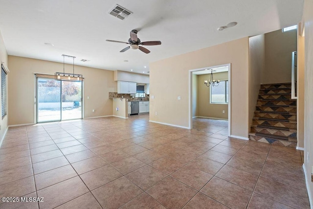 unfurnished living room with visible vents, baseboards, ceiling fan with notable chandelier, stairs, and light tile patterned flooring