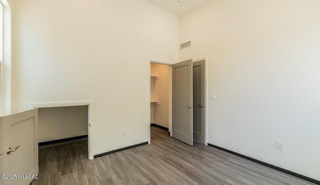 4270 E Broadway Blvd, Tucson, AZ 85711 - unfurnished bedroom with visible vents, wood finished floors, baseboards, a walk in closet, and a high ceiling