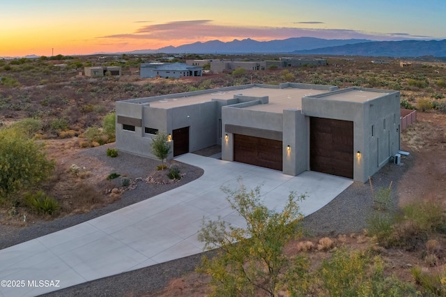 pueblo-style house with a garage, a mountain view, stucco siding, and driveway