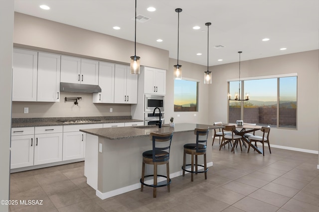 kitchen featuring visible vents, baseboards, under cabinet range hood, stainless steel appliances, and an island with sink