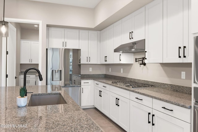 kitchen with white cabinetry, under cabinet range hood, a sink, dark stone countertops, and stainless steel appliances