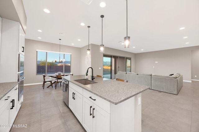 kitchen featuring light stone countertops, appliances with stainless steel finishes, a notable chandelier, a sink, and light tile patterned floors
