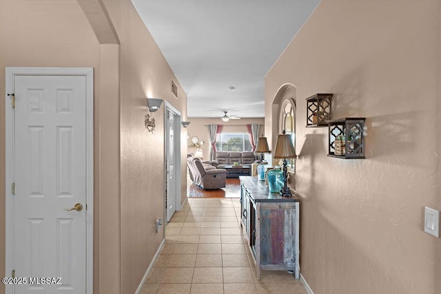 corridor with arched walkways, baseboards, visible vents, and light tile patterned flooring