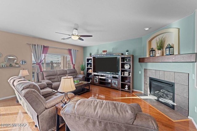 living room featuring a ceiling fan, baseboards, a tiled fireplace, and wood finished floors