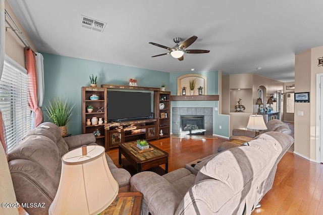 living area with ceiling fan, a fireplace, baseboards, wood finished floors, and visible vents