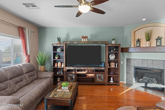 living room with a tiled fireplace, a ceiling fan, wood finished floors, and visible vents