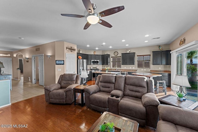 living room featuring ceiling fan, visible vents, arched walkways, light wood-style floors, and recessed lighting