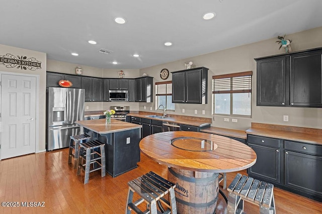 kitchen featuring recessed lighting, a center island, dark cabinets, a sink, and appliances with stainless steel finishes