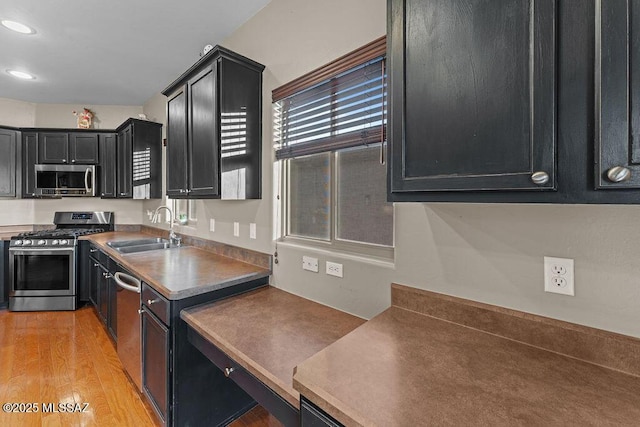 kitchen with appliances with stainless steel finishes, a sink, light wood finished floors, dark cabinetry, and recessed lighting