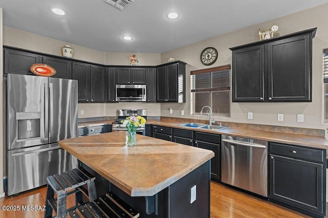 kitchen featuring a breakfast bar area, visible vents, a sink, dark cabinets, and stainless steel appliances