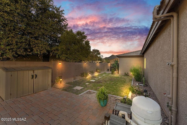 patio terrace at dusk with a lawn and a fenced backyard