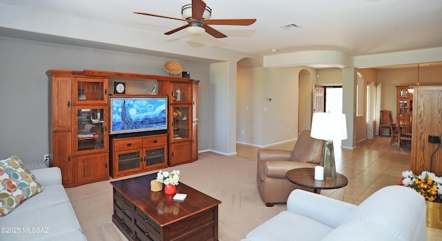 living area featuring ceiling fan, arched walkways, baseboards, light tile patterned floors, and visible vents