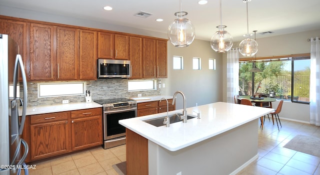 kitchen featuring brown cabinets, appliances with stainless steel finishes, a sink, light tile patterned floors, and tasteful backsplash