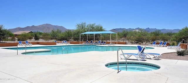 pool with a community hot tub, a patio area, a mountain view, and fence