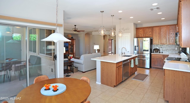kitchen with brown cabinetry, appliances with stainless steel finishes, arched walkways, a center island with sink, and a sink