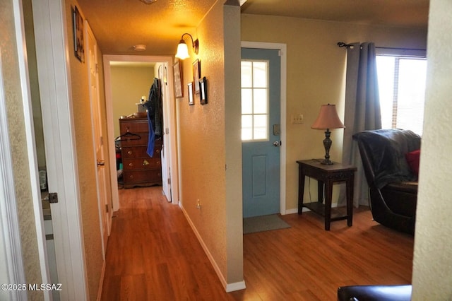 corridor with wood finished floors, plenty of natural light, and baseboards