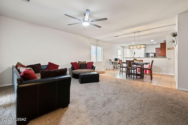 living room featuring baseboards, ceiling fan, light carpet, and light tile patterned flooring