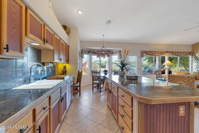 kitchen featuring visible vents, a center island, brown cabinets, a sink, and light tile patterned floors
