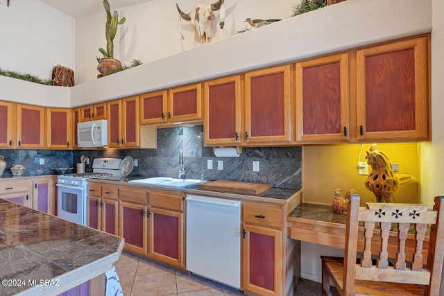 kitchen with decorative backsplash, a sink, light tile patterned floors, tile counters, and white appliances