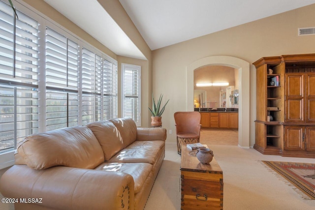 living room featuring baseboards, lofted ceiling, light colored carpet, and visible vents