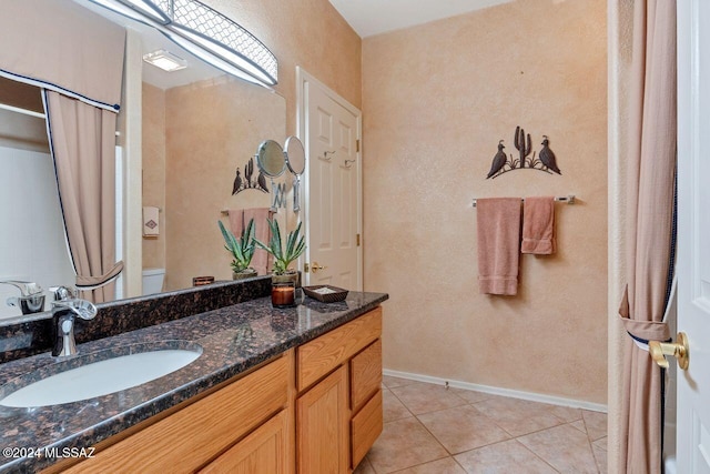 bathroom with tile patterned flooring, vanity, a textured wall, toilet, and baseboards