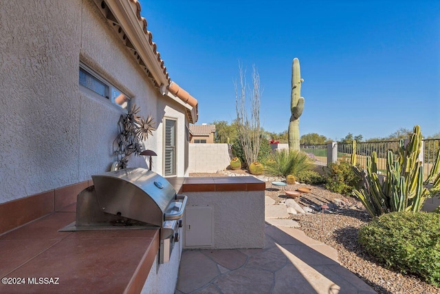 view of patio with exterior kitchen, fence, and a grill