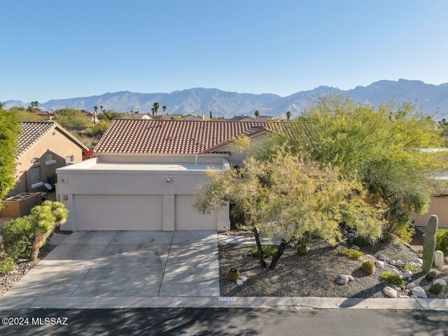 view of front of property featuring a tile roof, a garage, stucco siding, a mountain view, and driveway