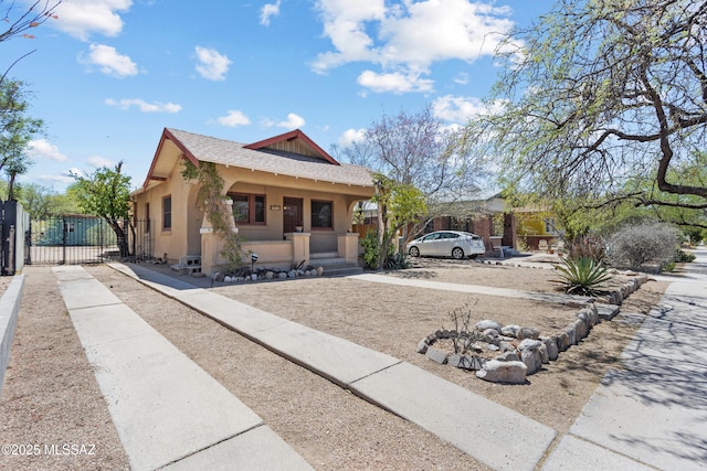 view of front of home featuring covered porch, roof with shingles, a gate, fence, and stucco siding