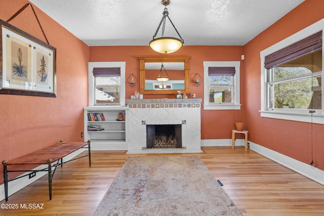 unfurnished room with baseboards, a fireplace with flush hearth, a healthy amount of sunlight, and wood finished floors