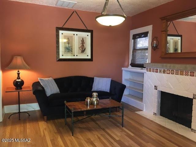 living area featuring visible vents, a textured ceiling, wood finished floors, and a tile fireplace