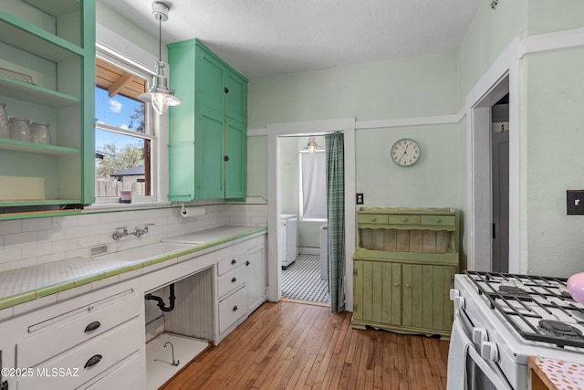 interior space featuring tasteful backsplash, a sink, white gas range, light wood-type flooring, and green cabinets