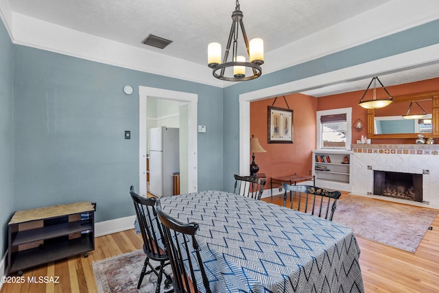 dining space with visible vents, baseboards, a chandelier, a tiled fireplace, and light wood-style flooring