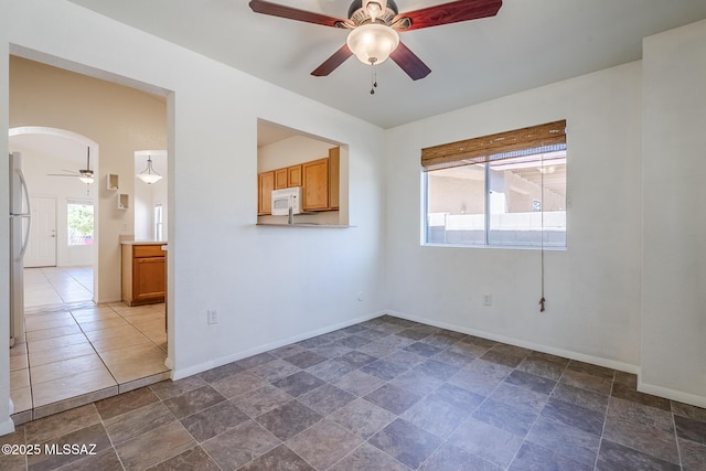 empty room featuring baseboards, stone finish floor, a ceiling fan, and arched walkways
